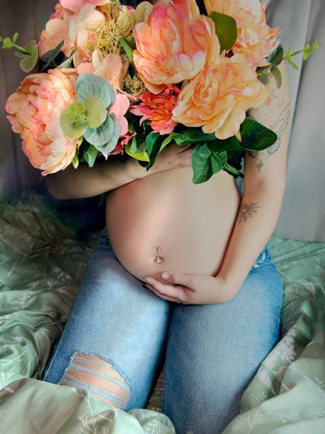 moody portrait of a pregnant young adult woman with flowers. - pierced abdomen flower beauty imagens e fotografias de stock