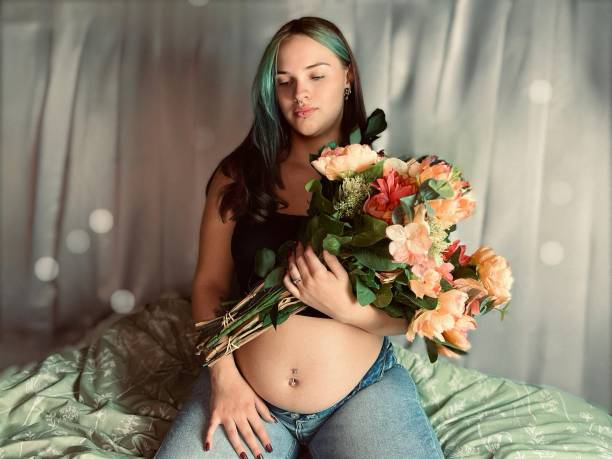 花束を持った妊娠中の若い成人女性の不機嫌な肖像画。 - pierced abdomen flower beauty ストックフォトと画像