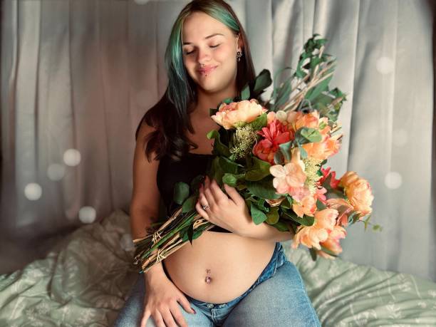 花束を持った妊娠中の若い成人女性の不機嫌な肖像画。 - pierced abdomen flower beauty ストックフォトと画像