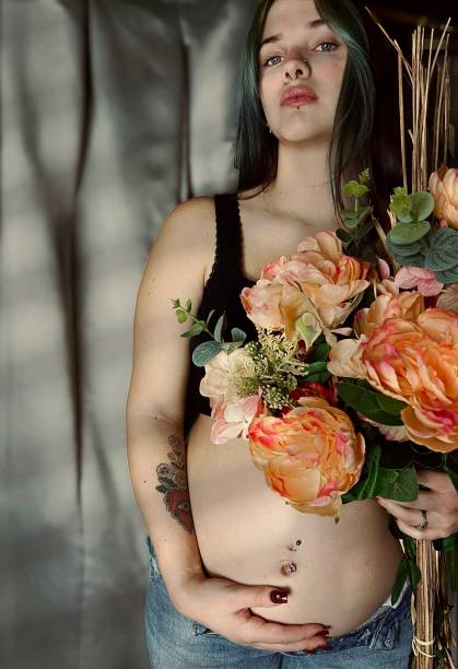 moody portrait of a pregnant young adult woman holding a bouquet of flowers. - pierced abdomen flower beauty imagens e fotografias de stock