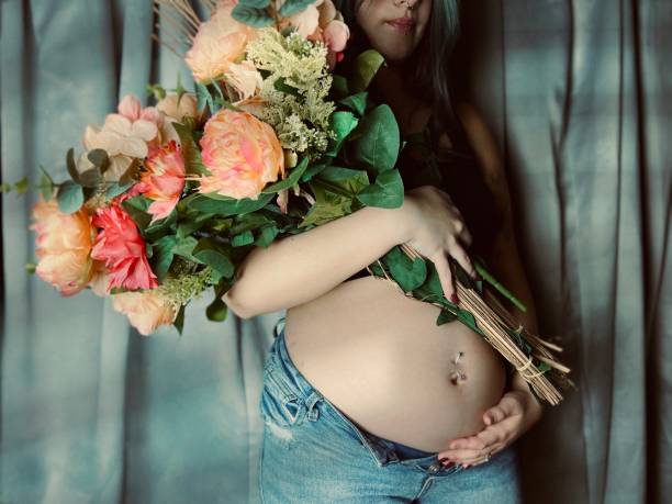 moody portrait of a pregnant young adult woman holding a bouquet of flowers. - pierced abdomen flower beauty ストックフォトと画像