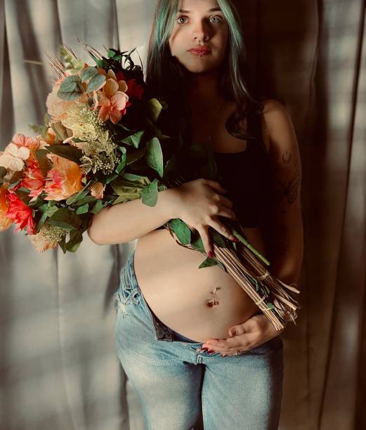 retrato mal-humorado de uma mulher adulta jovem grávida segurando um buquê de flores. - pierced abdomen flower beauty - fotografias e filmes do acervo