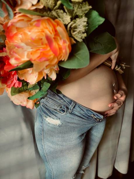 花束を持った妊娠中の若い成人女性の不機嫌な肖像画。 - pierced abdomen flower beauty ストックフォトと画像