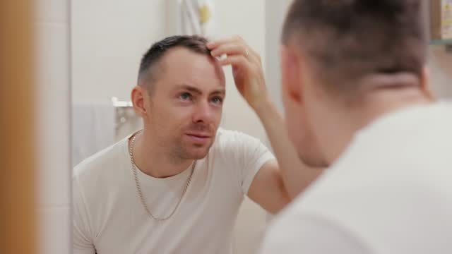 A man looks at his baldness in the mirror and is dissatisfied with it