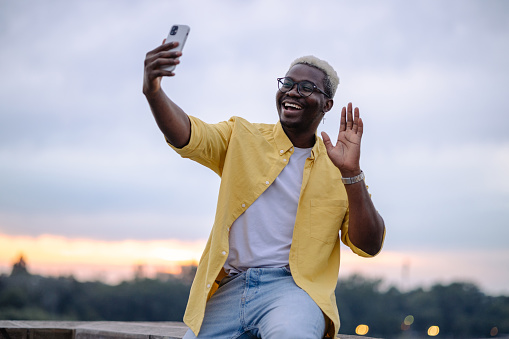 A young African American man using a smart phone in the city and smiling. He is taking selfie