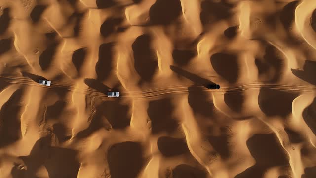 The drone is flying up looking topdown at three cars driving through the Sahara desert in Tunisia Aerial Footage 4K
