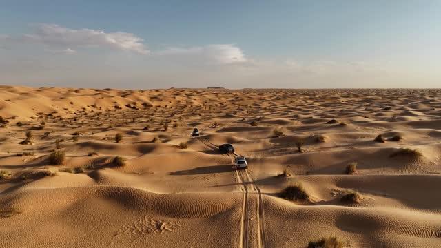 The drone is flying up looking at three cars driving through the Sahara desert in Tunisia Aerial Footage 4K