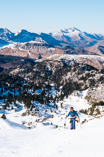 a woman mountaineer ascends a slope in winter mountain, in the background landscape of many Pyrenees mountains