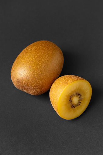 Whole and halved ripe golden kiwi isolated on a black background. Kiwi with yellow juicy sweet pulp (Actinidia chinensis).