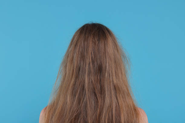 Woman with damaged hair on light blue background, back view