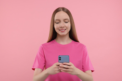 Happy young woman using smartphone on pink background