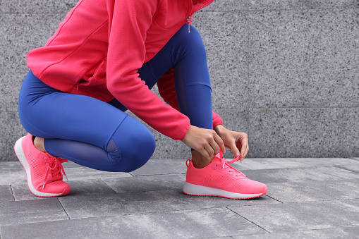 Woman in gym clothes tying shoelace of sneakers on street, closeup