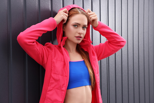 Beautiful woman in gym clothes posing near dark grey wall on street