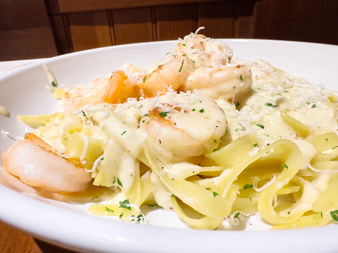 Tagliatelle pasta dish with shrimp sauce and shredded parmesan on a restaurant table
