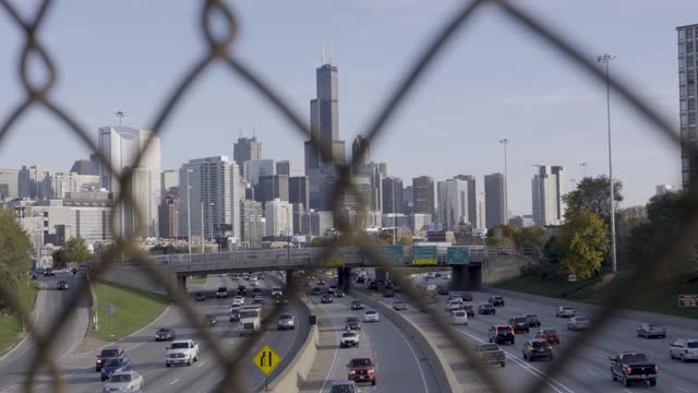 Downtown Chicago skyline and highway traffic, viewed through a fence in daylight
