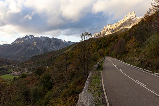 Landscape of Picos de Europa national park road through autumn forest with bright colorful leaves and sunset in northern Spain