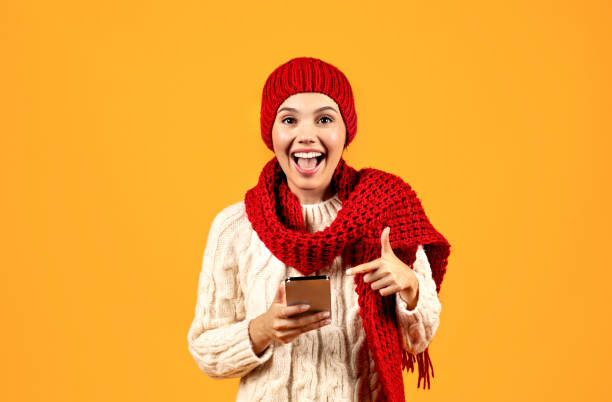 istock Excited Young Woman Pointing At Phone On Yellow Studio Background 1925646039