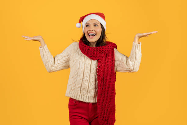 istock woman in Santa hat spreading arms open on yellow backdrop 1925646071