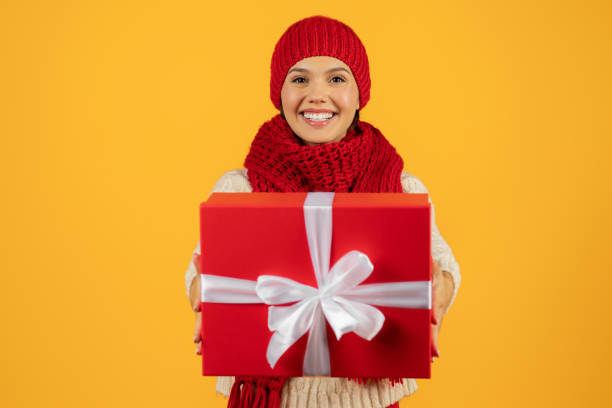 istock woman in winter attire showing wrapped New Year gift, studio 1925646073