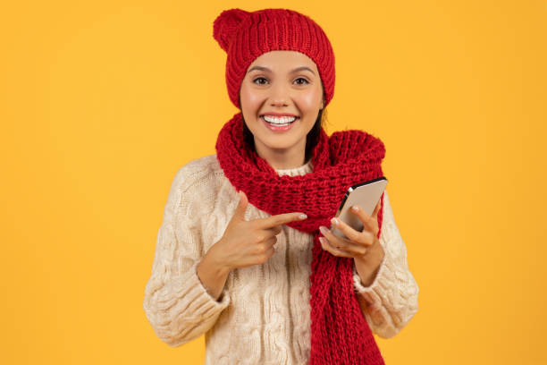 istock Happy lady in hat pointing at smartphone on yellow backdrop 1925646076