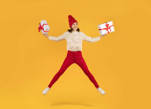 istock Cheerful woman in knitwear leaps holding two gift boxes, studio 1925646693