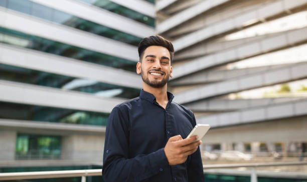 istock Modern Arabian millennial businessman using mobile phone near urban building 1925672050