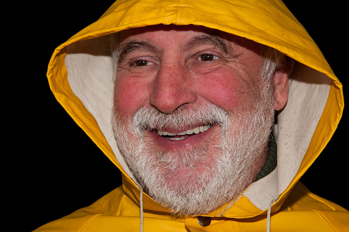 The old fisherman with a shaggy beard, yellow rain jacket and hood laughs, while the wrinkles around his eyes reveal a life story full of experiences.