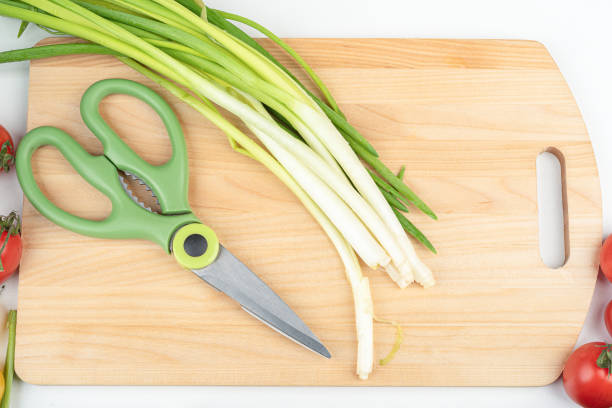 Green onions and kitchen scissors on a wooden cutting board. Home cooking.
