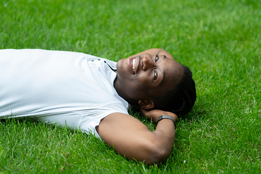 a close up young african american person lying and chilling on the grass in the park