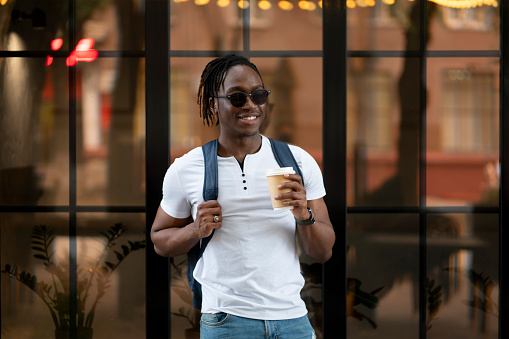 a stylish black man in white t-shirt drinking coffee in takeaway cup in the city