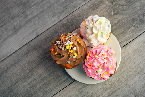 An overhead view of three tasty cupcakes on a plate on a table top.