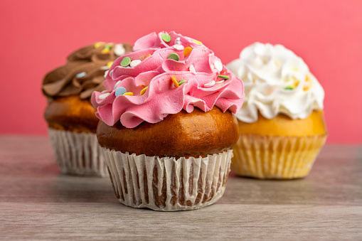 A close up of three tasty cupcakes on a pink background.