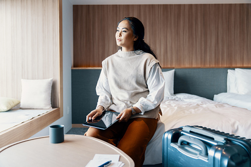 Young businesswoman looking out her hotel window while on a business trip