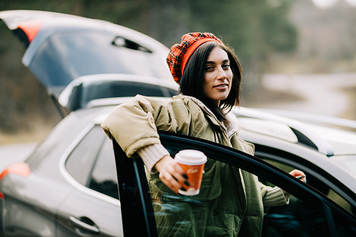 Portrait of a beautiful young fashionable woman enjoying a winter road trip and drinking coffee to go on a lovely cold day