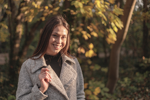 Portrait of a beautiful young woman holding bouquet of dry autumn leafs and smiling