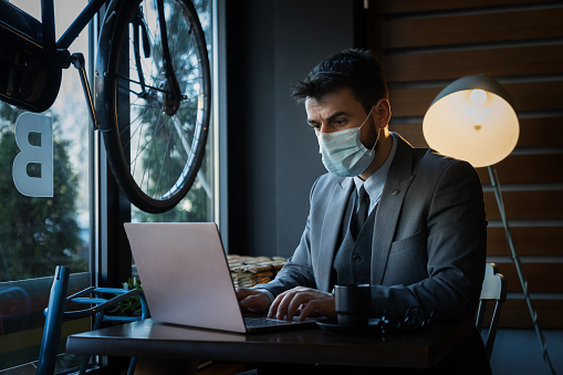 Young businessman wearing a protective face mask using his laptop in a coffee shop