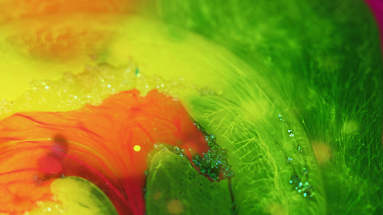 Color fluid. Ink water mix. Neon green yellow orange dye blend flow glitter texture paint blob floating art abstract background.