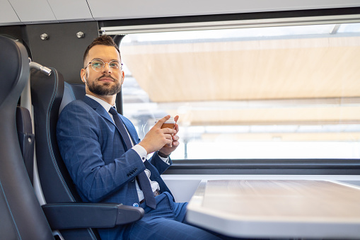 A businessman is holding a cup of coffee while  traveling in a train on his way to work,  relaxing