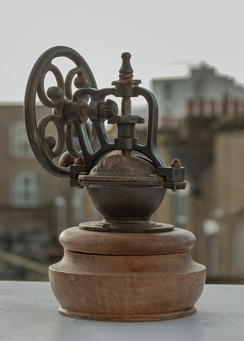 London, UK - Oct 17, 2023 - Antique coffee bean original grinder metal shake wheel with hand crank. Old original coffee grinder with traces of time and scuffs on the body, Space for text, Selective focus.