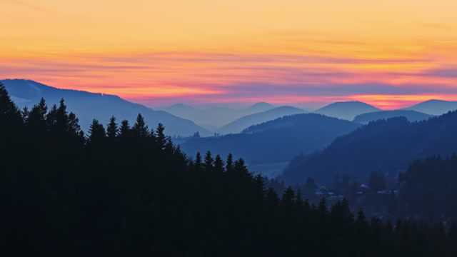 AERIAL Drone Shot of Beautiful Silhouette Coniferous Trees and Foggy Mountains under Orange Sky during Golden Hour in Winter in Rogla, Slovenia