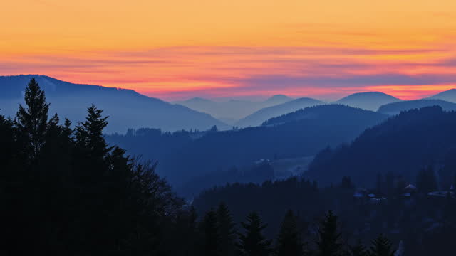 AERIAL Drone Shot of Amazing Silhouette Coniferous Forest and Foggy Mountain Ranges under Orange Sky During Golden Hour in Winter in Rogla, Slovenia