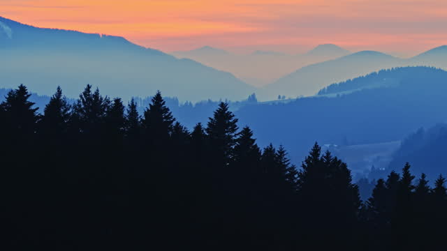 AERIAL Drone Shot of Picturesque View of Silhouette Coniferous Forest and Foggy Mountains under Orange Sky During Golden Hour in Rogla, Slovenia