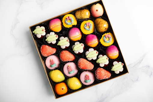 Box of rainbow marzipan sweets in form of different fruits and cakes