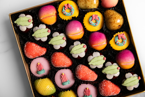 Box of rainbow marzipan sweets in form of different fruits and cakes