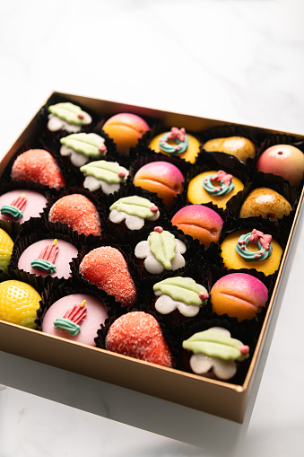 Box of rainbow marzipan sweets in form of different fruits and cakes