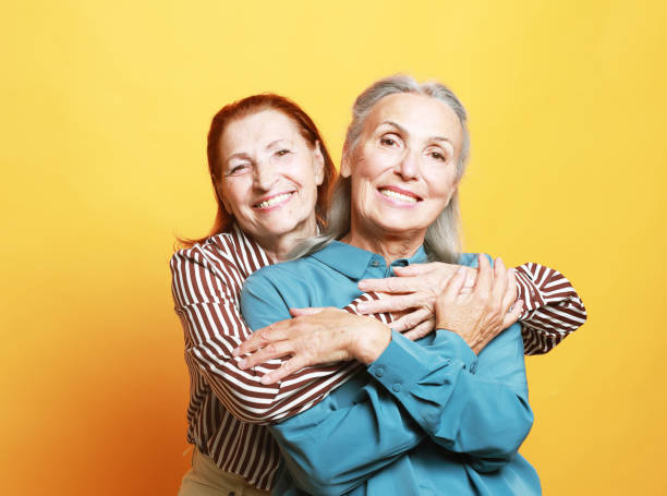 istock Two elderly women friends hugging on yellow background. 1926126097