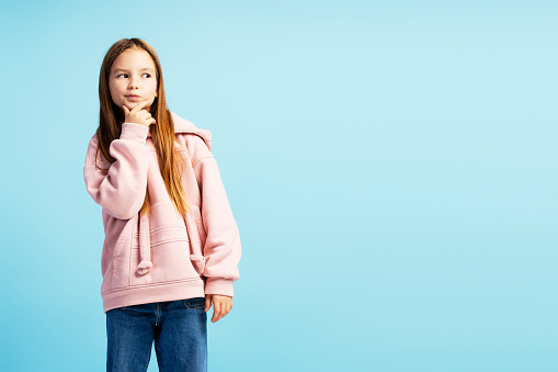 Portrait of beautiful little girl thinking, choosing something, looking away on copy space isolated on blue background. Concept of shopping, discounts