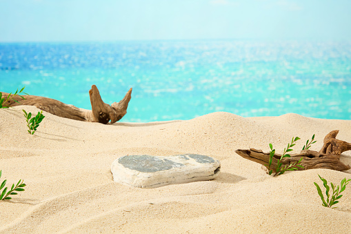Blue sea filled with sunshine, a block of stone on sand background with dry twigs and green grass. Empty space on stone for sunscreen product presentation. Front view