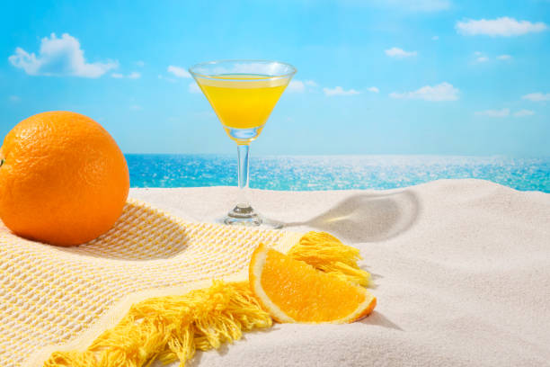 istock Front view of fresh oranges, a cocktail and a tablecloth placed on white sand with sunshine. Tropical atmosphere creates a relaxing feeling. Copy space. 1926207269