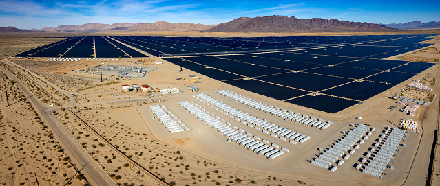 Aerial view of industrial battery units storing electricity.  In the distance is a huge area of solar panels and mountains.